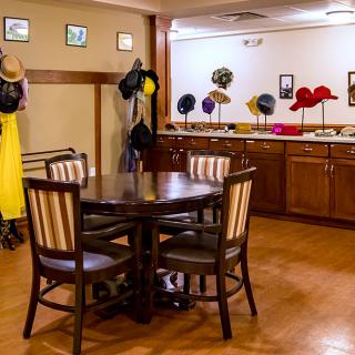 A cozy dining area with a variety of hats on display and coats hanging, featuring a table and chairs on a wooden floor.
