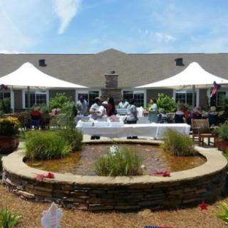 An outdoor gathering with people seated under tents by a garden fountain.