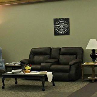 A cozy living room featuring a dark sofa, armchair, coffee table with decorative items, and a table lamp.