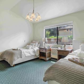 A cozy bedroom with twin beds, natural light from the window, and a modern chandelier.