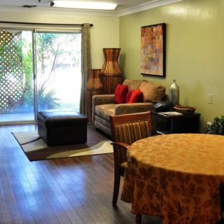 A cozy living room with a sofa, table, and wood flooring, featuring a sliding door leading outside.