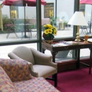 A cozy lobby area with a sofa, chair, and table near large windows overlooking an outdoor patio.