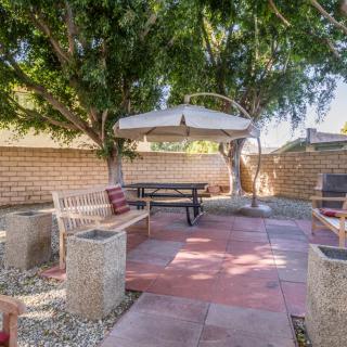 A cozy backyard patio with a picnic table and umbrella, surrounded by trees and a brick wall.