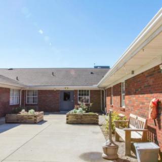 A sunny courtyard with benches and potted plants in front of a brick building.