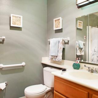 A neatly organized bathroom with a toilet, sink, and mirror, featuring decorative wall art and towels.