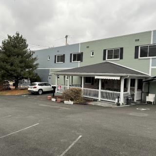 A view of a residential building with a covered entrance and parking area under a cloudy sky.