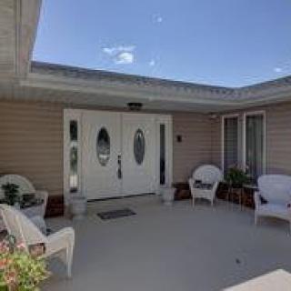 A cozy outdoor patio with white chairs and plants leading to a double door entrance.