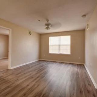 An empty room with hardwood flooring, a ceiling fan, and a window.
