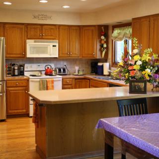 A modern kitchen featuring wooden cabinets, a central island with a countertop, and vibrant flower arrangements.