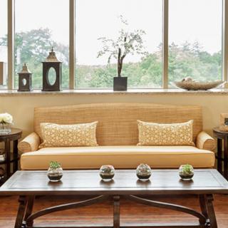 A cozy living room featuring a beige sofa with decorative pillows, complemented by a wooden coffee table and indoor plants near large windows.