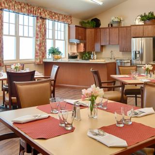 A well-set dining area with tables and chairs, adjacent to a kitchen space.