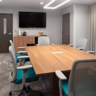 A modern conference room with a wooden table, ergonomic chairs, and a large TV screen.