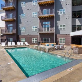 An outdoor swimming pool surrounded by lounge chairs in front of a modern apartment building with multiple balconies.
