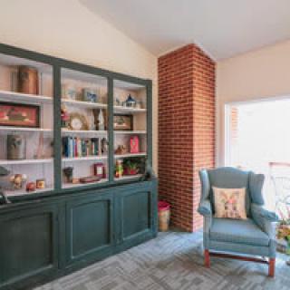A cozy living room with a bookshelf and armchair by a brick chimney.