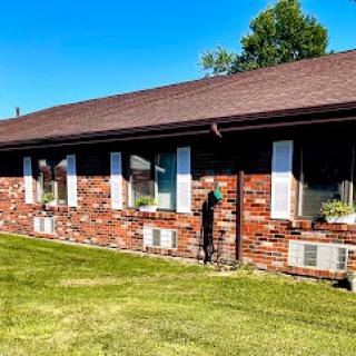 A well-maintained brick house with large windows and a lush green lawn under a clear blue sky.