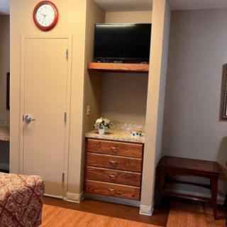 A cozy interior room with a wall-mounted TV, dresser, and analog clock.