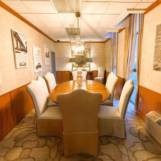 A well-lit dining room with a long table surrounded by upholstered chairs, adorned with artwork on the walls.