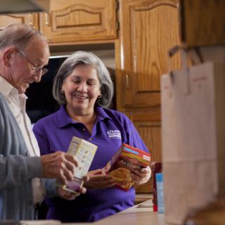 An elderly man and a woman are organizing groceries in a kitchen.