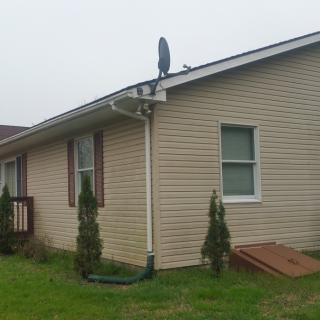 A single-story house with a satellite dish mounted on the roof and small bushes along the side.