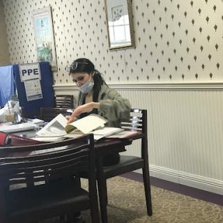 A person reading and studying at a table filled with books in an indoor workspace.