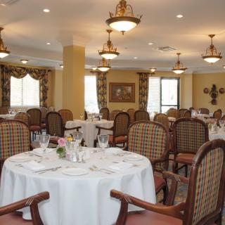 An elegant dining room with neatly arranged tables and chairs, illuminated by chandeliers.