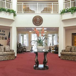 A spacious and elegantly decorated lobby with sofas, a central table holding a plant, red carpeting, and natural lighting.