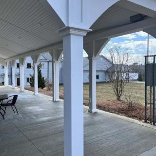 A spacious covered patio with columns and outdoor seating overlooks a grassy residential area under a cloudy sky.