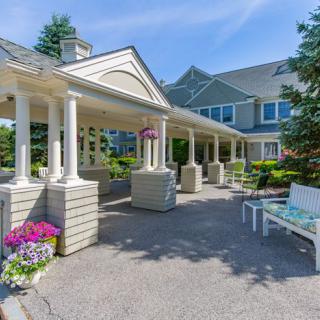 A well-maintained building entrance with columns, surrounded by flowers and a bench.