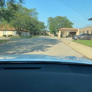 A car's perspective driving through a quiet residential street on a sunny day.
