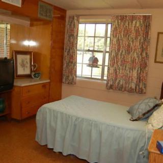 A cozy bedroom with a single bed, a window with patterned curtains, and a wall-mounted television.