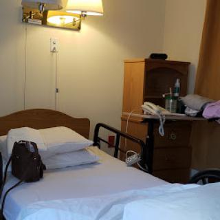A simple hospital room with a bed, lamp, and a nightstand holding various personal items.