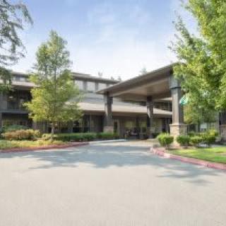 A spacious building entrance surrounded by trees and a curved driveway.