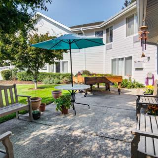 A cozy outdoor patio area with benches, a table, and a blue umbrella set amidst a garden.