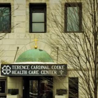 Entrance to Terence Cardinal Cooke Health Care Center with a prominent sign and surrounding trees.