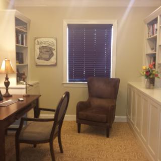 A cozy home office with a desk, chairs, bookshelves, and a window.