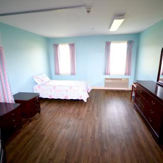 A minimalist bedroom with a single bed, wooden floors, and pastel-colored walls.