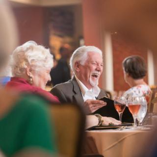 Elderly couple laughing and enjoying a meal at a restaurant.