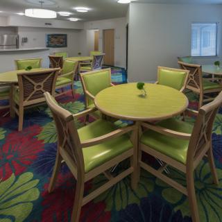 A modern dining area with green chairs and round tables set against a colorful carpet.