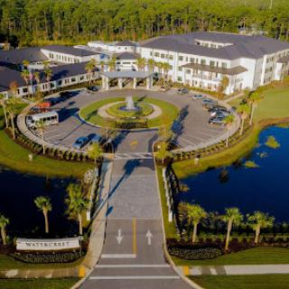 Aerial view of a modern resort with a fountain, surrounded by ponds and palm trees.