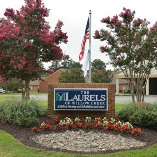 Entrance to The Laurels of Willow Creek with manicured landscaping and an American flag.