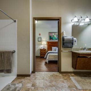An accessible hotel room showcasing a modern bathroom with a view into the cozy bedroom area.
