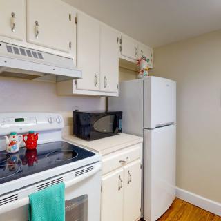 A compact kitchen with white cabinets, featuring a refrigerator, microwave, and oven.