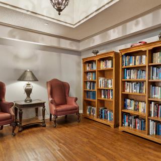 A cozy library corner featuring bookshelves, comfortable chairs, and a lamp for reading.