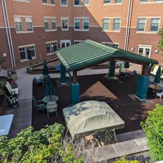 A serene courtyard featuring a green pavilion and comfortable seating surrounded by brick buildings.
