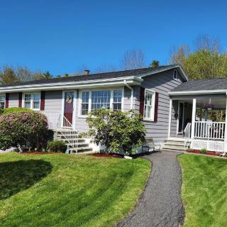 A cozy, gray single-story house with a well-maintained lawn and garden under a clear blue sky.