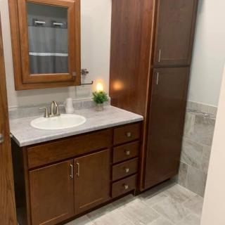 A modern bathroom featuring a wooden vanity with a marble countertop and a built-in sink, complemented by a tall cabinet and a mirror above.