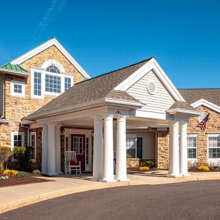 A well-maintained building with a central entrance featuring columns and a stone exterior, set against a clear blue sky.