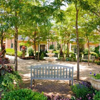 A peaceful garden with a bench, surrounded by trees and a central fountain.