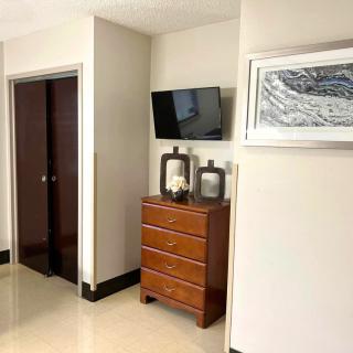 A modern bedroom corner featuring a wooden dresser, a wall-mounted TV, and framed artwork.