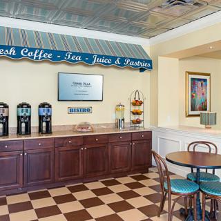 A cozy coffee and beverage station with a checkered floor, featuring self-service options for coffee, tea, juice, and pastries.